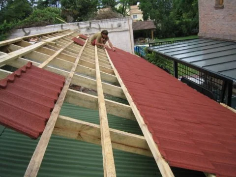 Instalador colocando tejas gravilladas sobre el techo de chapa existente